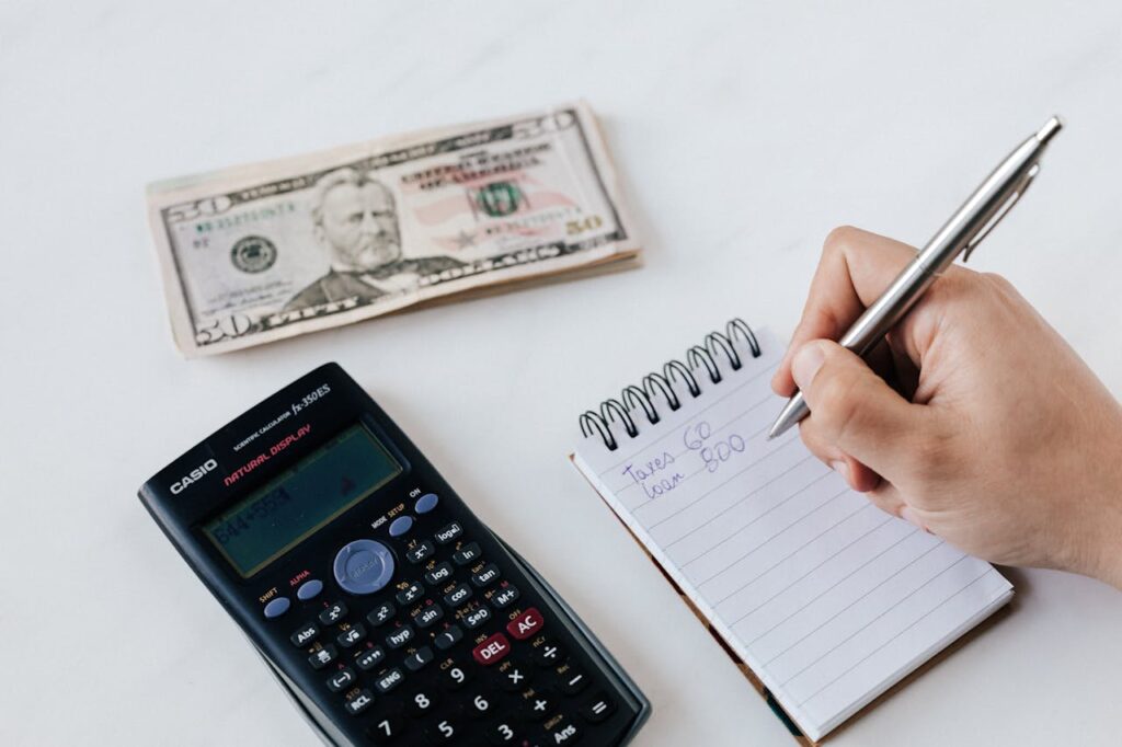 The 4 Digital Products That Will Make You Consistent Money Online in 2026 Close-up of budgeting items including calculator, cash, and notebook for financial planning.